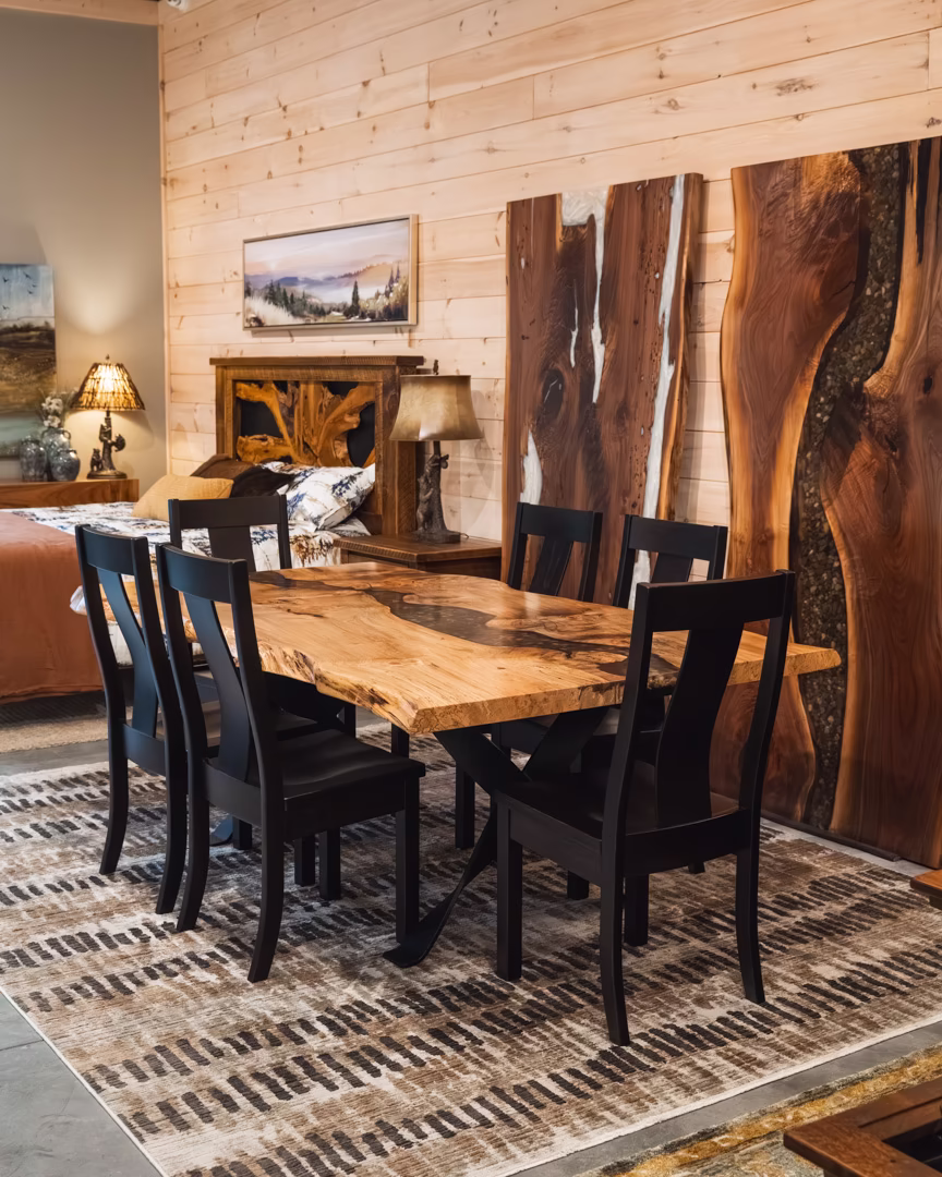 new (368 of 396) A live-edge wood dining table with a resin river inlay and black chairs, set on a textured rug in a rustic room with wood-paneled walls.