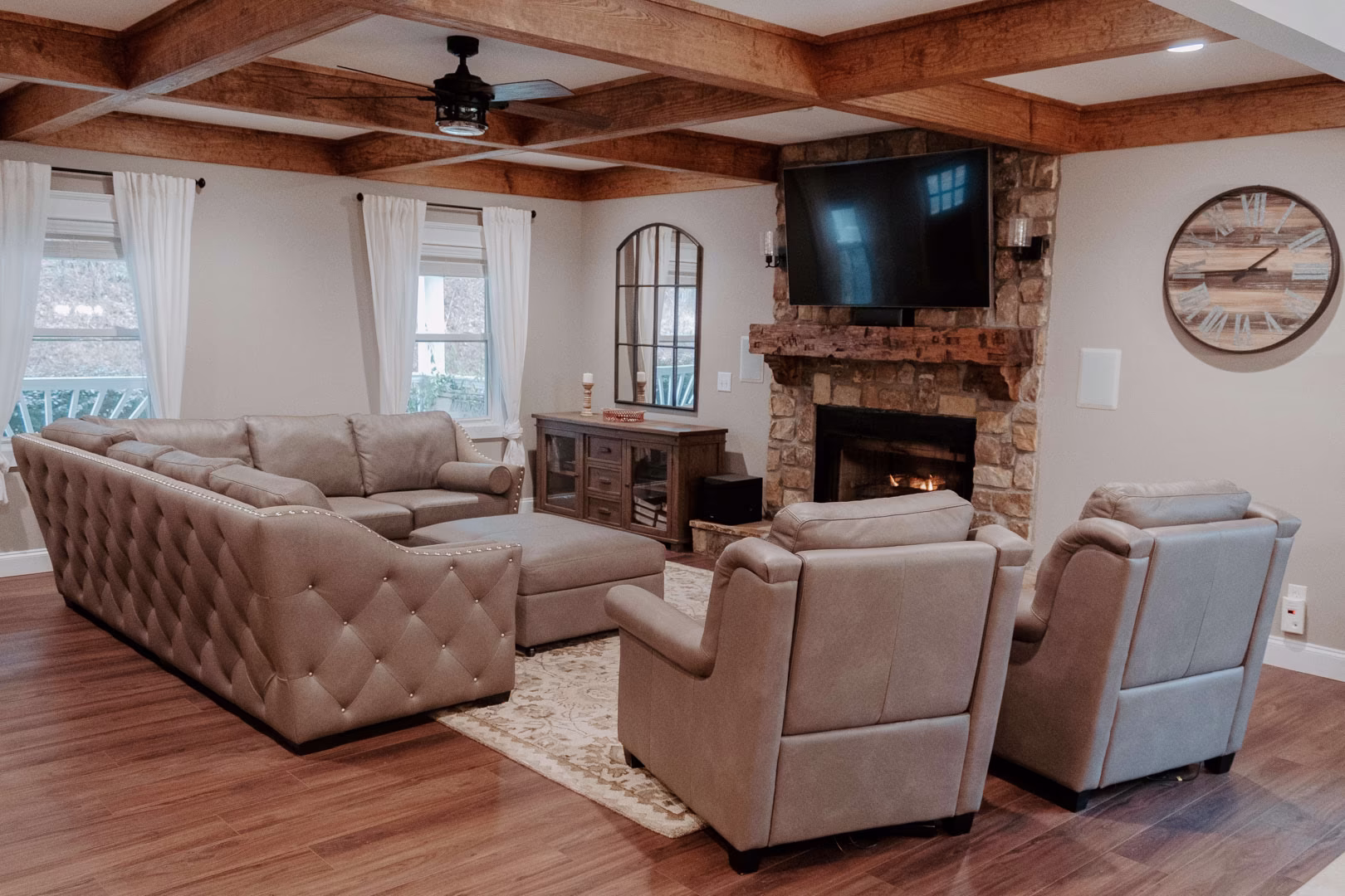 new (128 of 396) A beige sectional sofa, two matching armchairs, and a stone fireplace with a flat screen TV occupy a cozy living room, complemented by a wooden coffee table, rug, and clock.