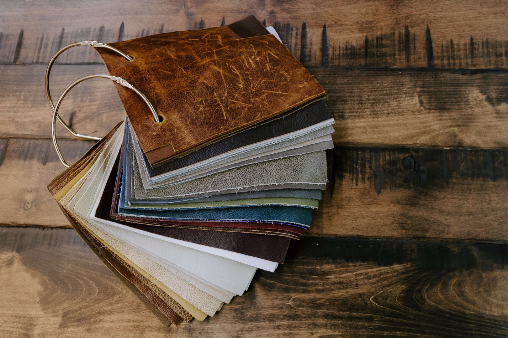new (266 of 396) A wooden surface displays a harmoniously stacked pile of leather samples, featuring various shades of brown, gray, and white with a noticeable green sample.