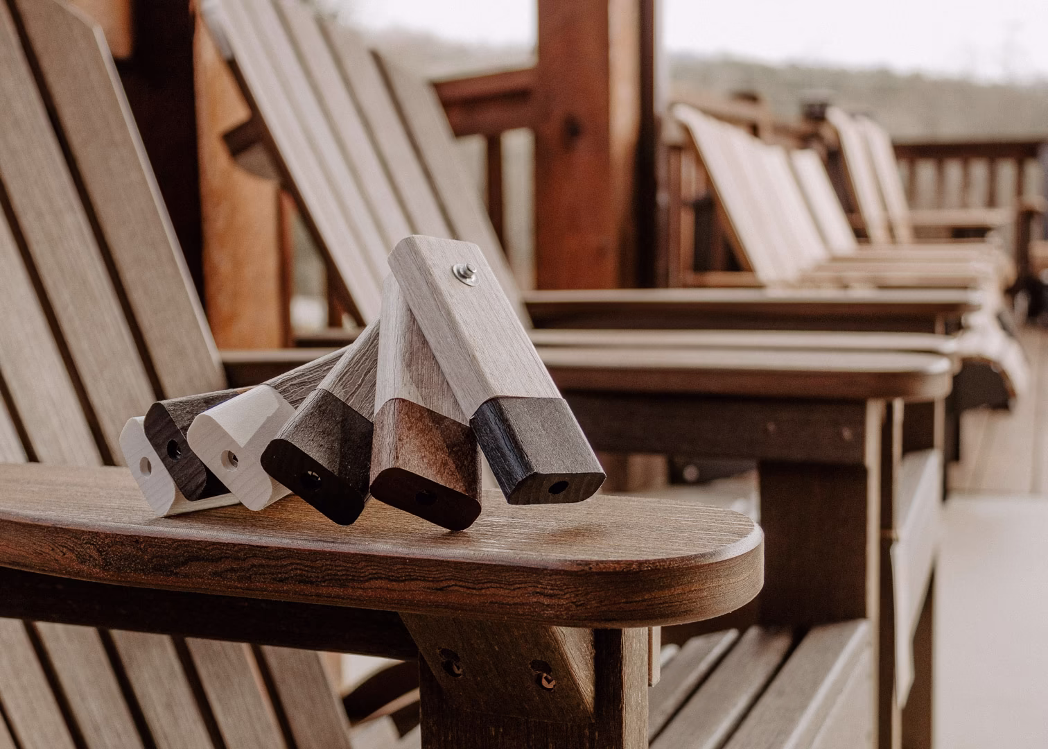 new (332 of 396) Six identical wooden chairs, with curved backrests and armrests, line a wooden deck, displaying a gradient of brown tones and one with a single silver knob.