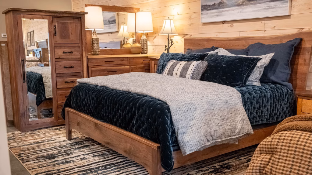 arden-live-wood-collection-featured-image A wooden bed with blue and gray bedding, wooden nightstands, and a dresser with mirror is surrounded by wooden furniture and decor in a cozy bedroom.
