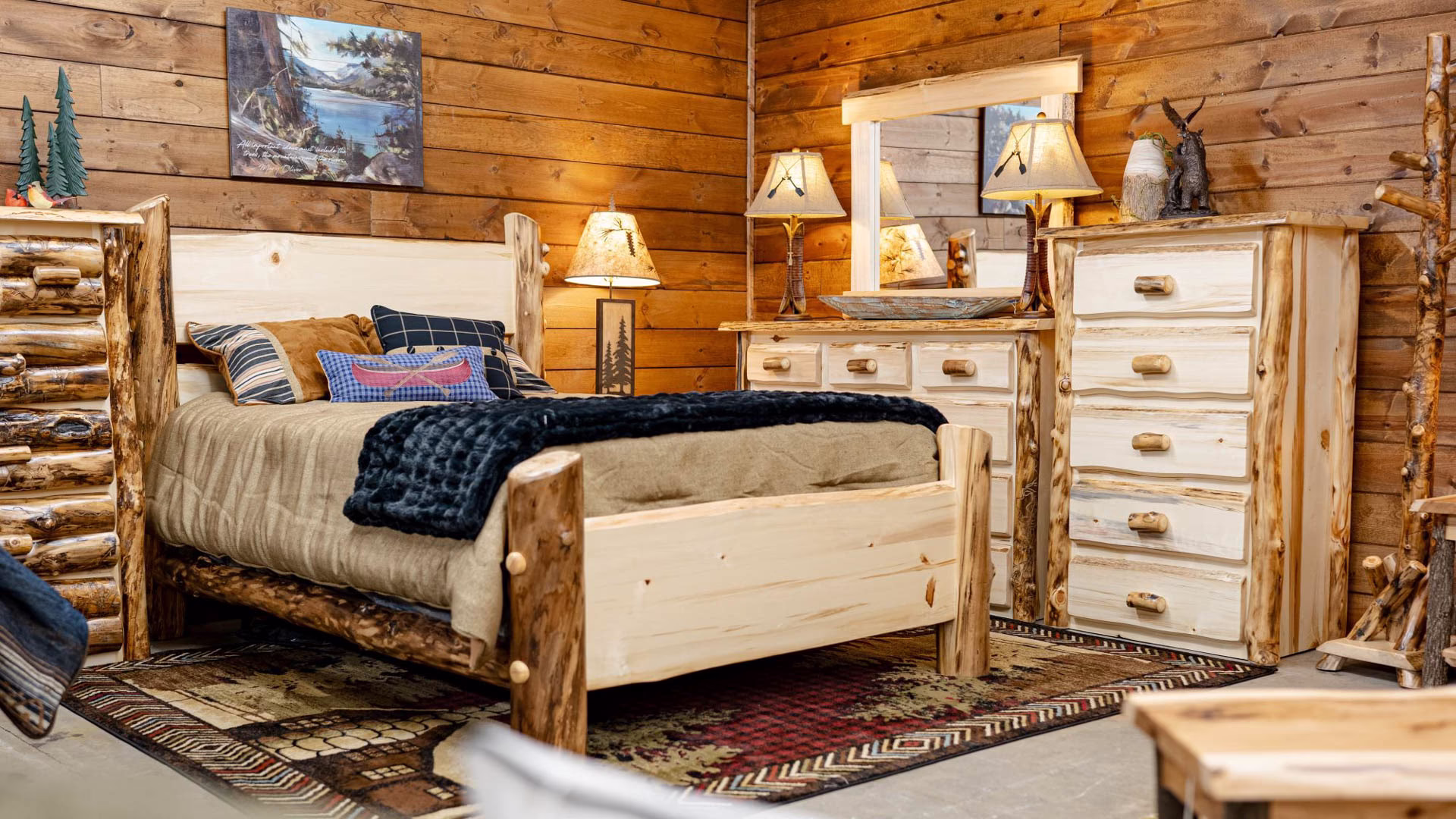 A rustic bedroom features a white wooden bed with a blue blanket, dresser, and nightstands, complemented by lamps, a painting, and a plant.
