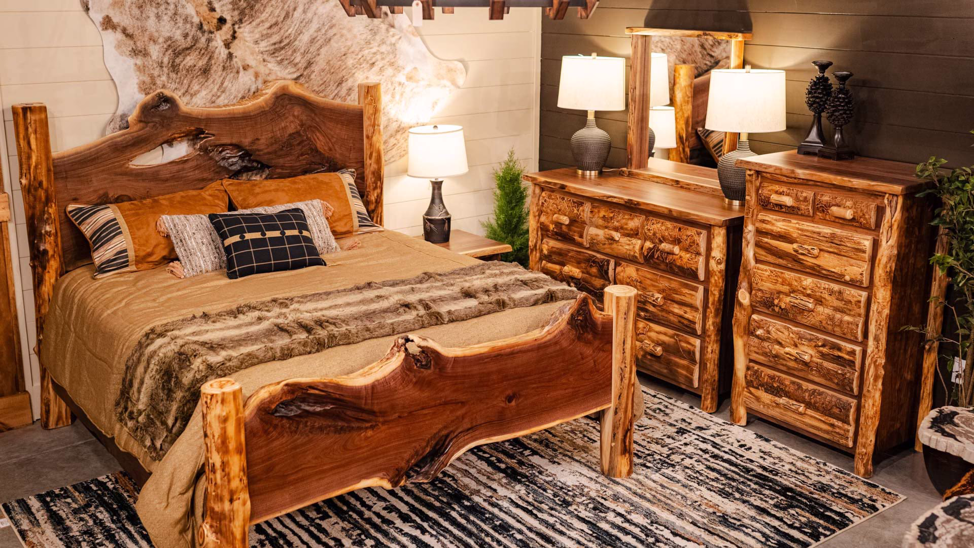 A rustic bedroom features a wooden dresser, nightstands, and a bed with a wooden headboard and footboard, set against a white wall and framed by a cowhide wallpaper.