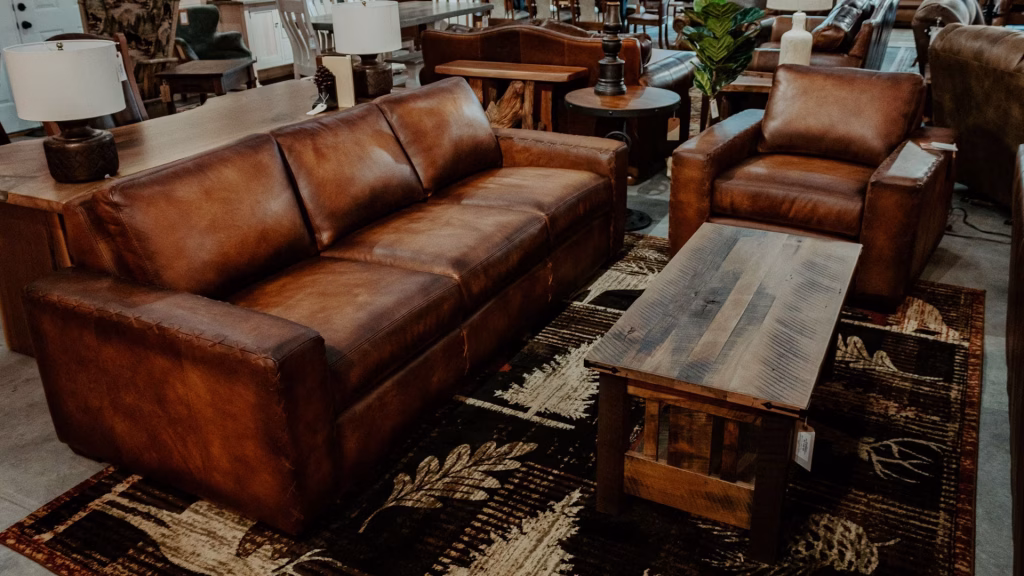 A brown leather sofa and armchair, accompanied by a wooden coffee table and two side tables, create a cozy gathering space in a furniture store.