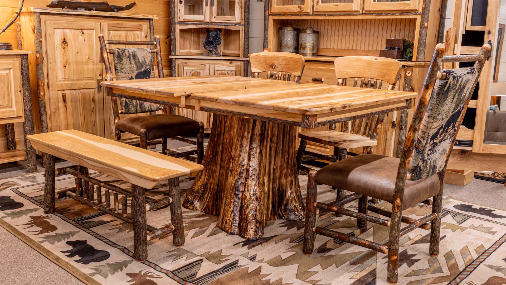 A wooden table with six chairs, a bench, and wooden cabinets fills a cozy cabin-themed room, complemented by a patterned rug and natural light.