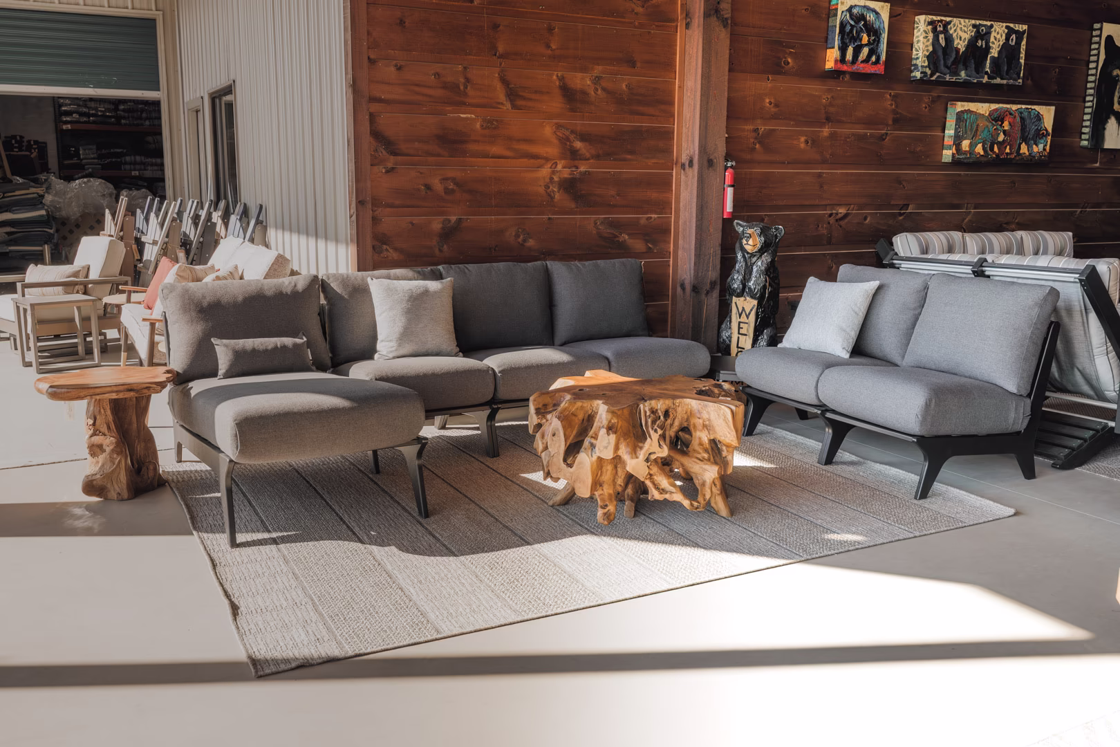hartley-collection-featured-image A modern gray sofa with wooden coffee table and side table, accompanied by a mirror and wooden wall decorations, is set against a gray rug in a room with natural light.