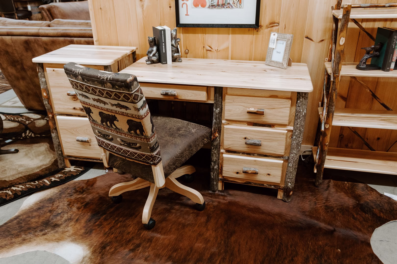 A cozy wooden room features a desk with a lamp, bookshelf, and chair, set against a wooden wall and cowhide rug.