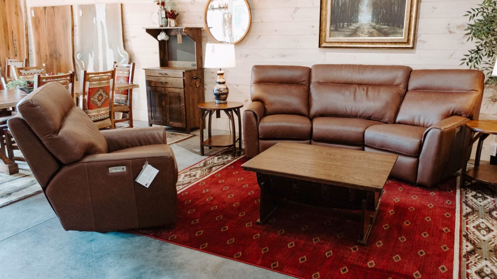 A brown leather recliner, sofa, and coffee table with red rug and white walls create a cozy and inviting living space.