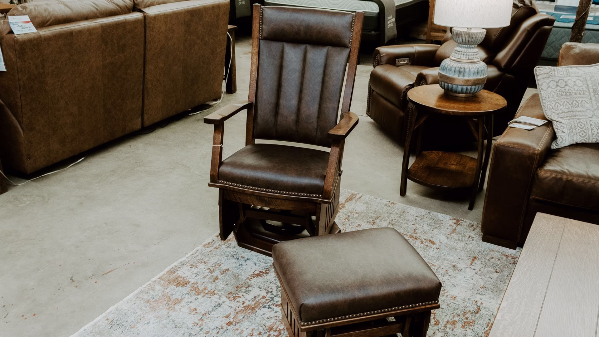A brown leather recliner with footrest and armrests is accompanied by two additional brown leather sofas in a furniture store, featuring a wooden floor and white rug.