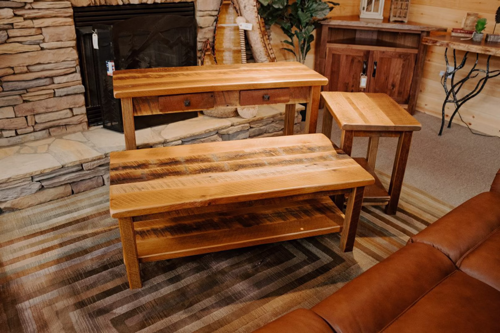 montana-barnwood-collection-featured-image Three reclaimed wood tables in a rustic setting showcase intricate carvings and variations in color and texture, accompanied by matching chairs and a fireplace.