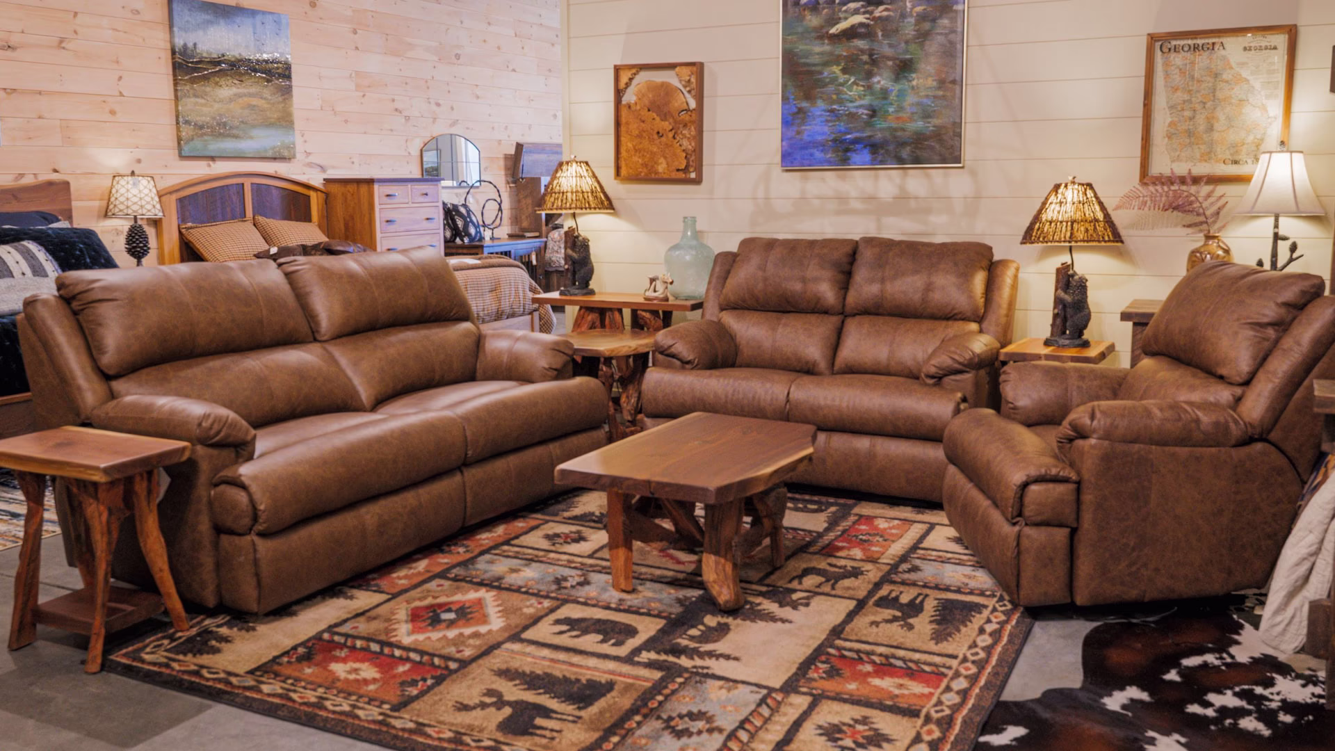 A cozy living room features two brown leather sofas, a wooden coffee table, a side table, a lamp, and a painting, with a cowhide rug and wooden walls.