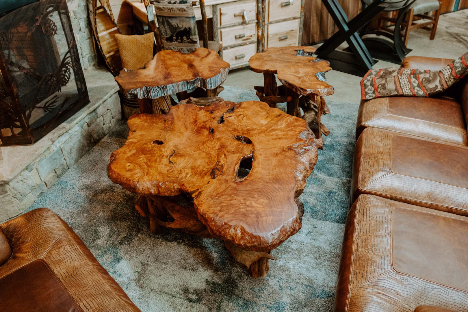 redwood-driftwood-collection-featured-image A wooden coffee table with three large holes sits in a cozy living room, accompanied by a leather couch, a fireplace, and a wooden bookshelf.