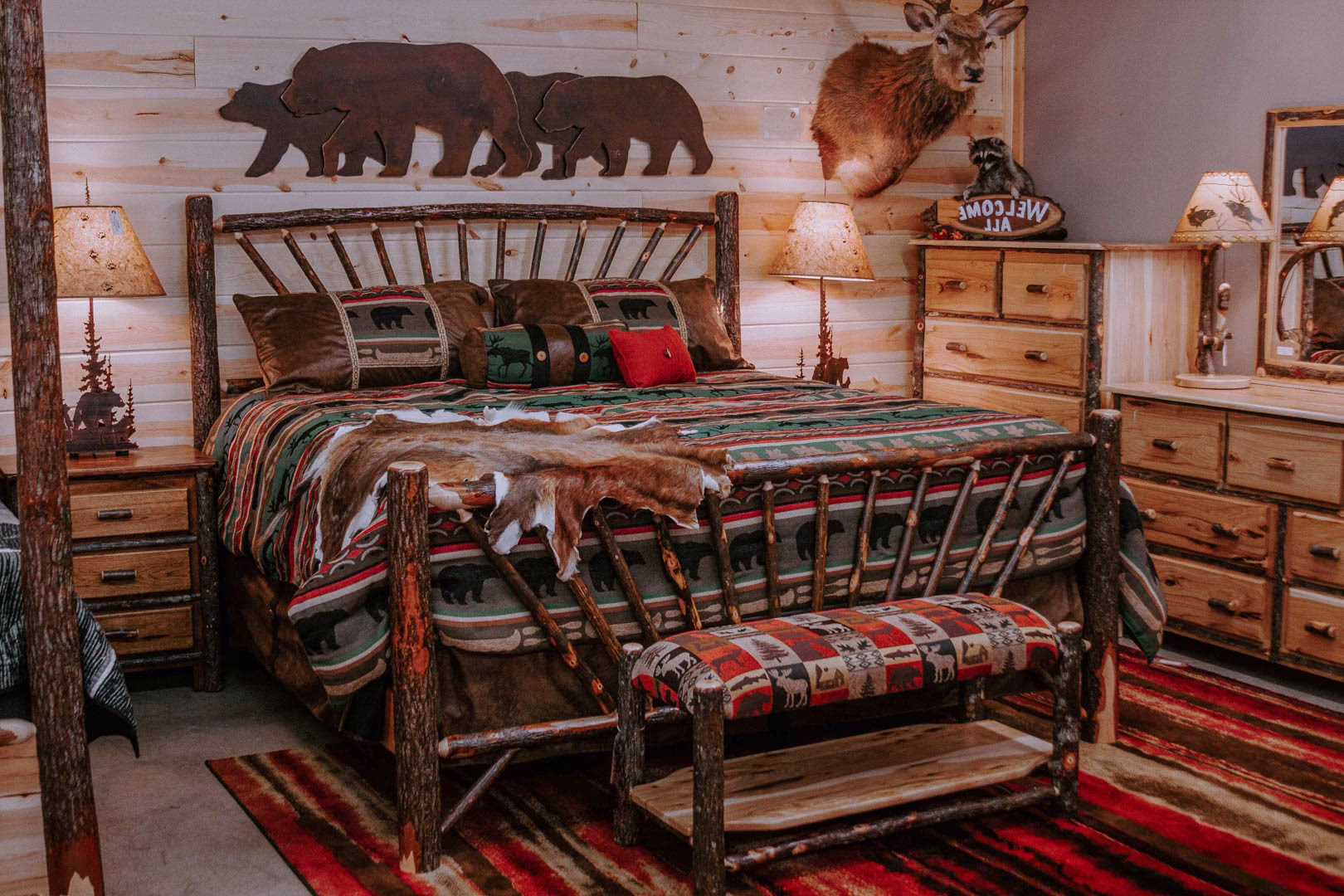 A rustic bedroom features a wooden bed with a colorful quilt, headboard, and footboard, accompanied by a wooden dresser, lamp, and wall decor.