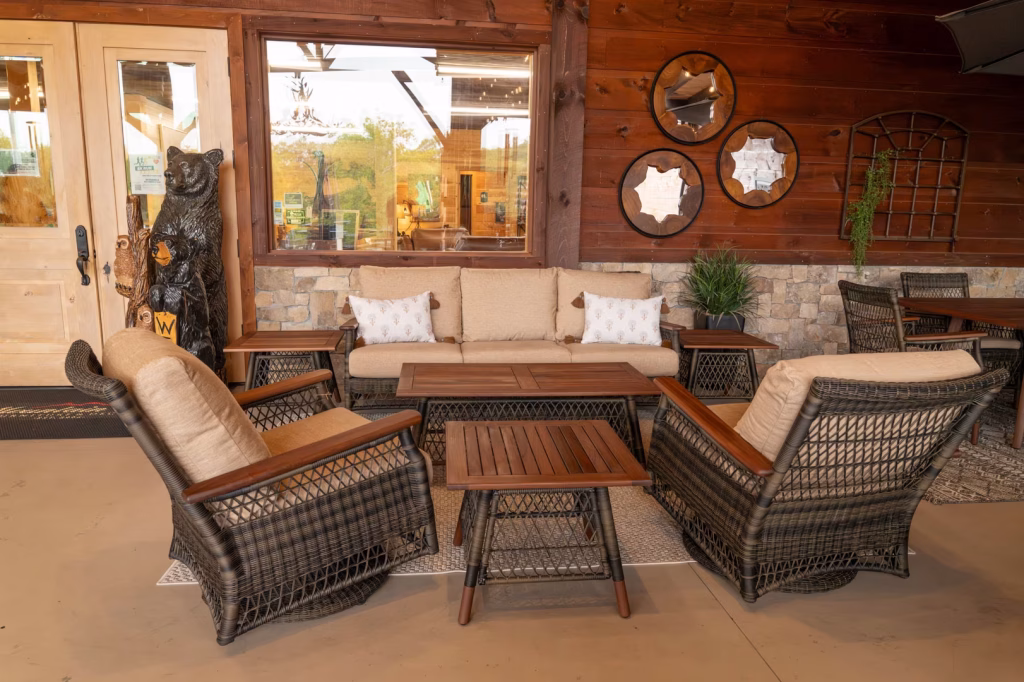 A wooden patio features a black bear statue, a beige sofa, white armchairs, and a coffee table, illuminated by natural light and a hanging plant.
