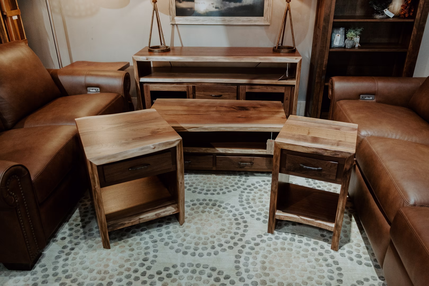 A furniture showroom displays a brown leather sofa, wooden coffee table, and end tables on scattered rugs, with a fireplace in the background.
