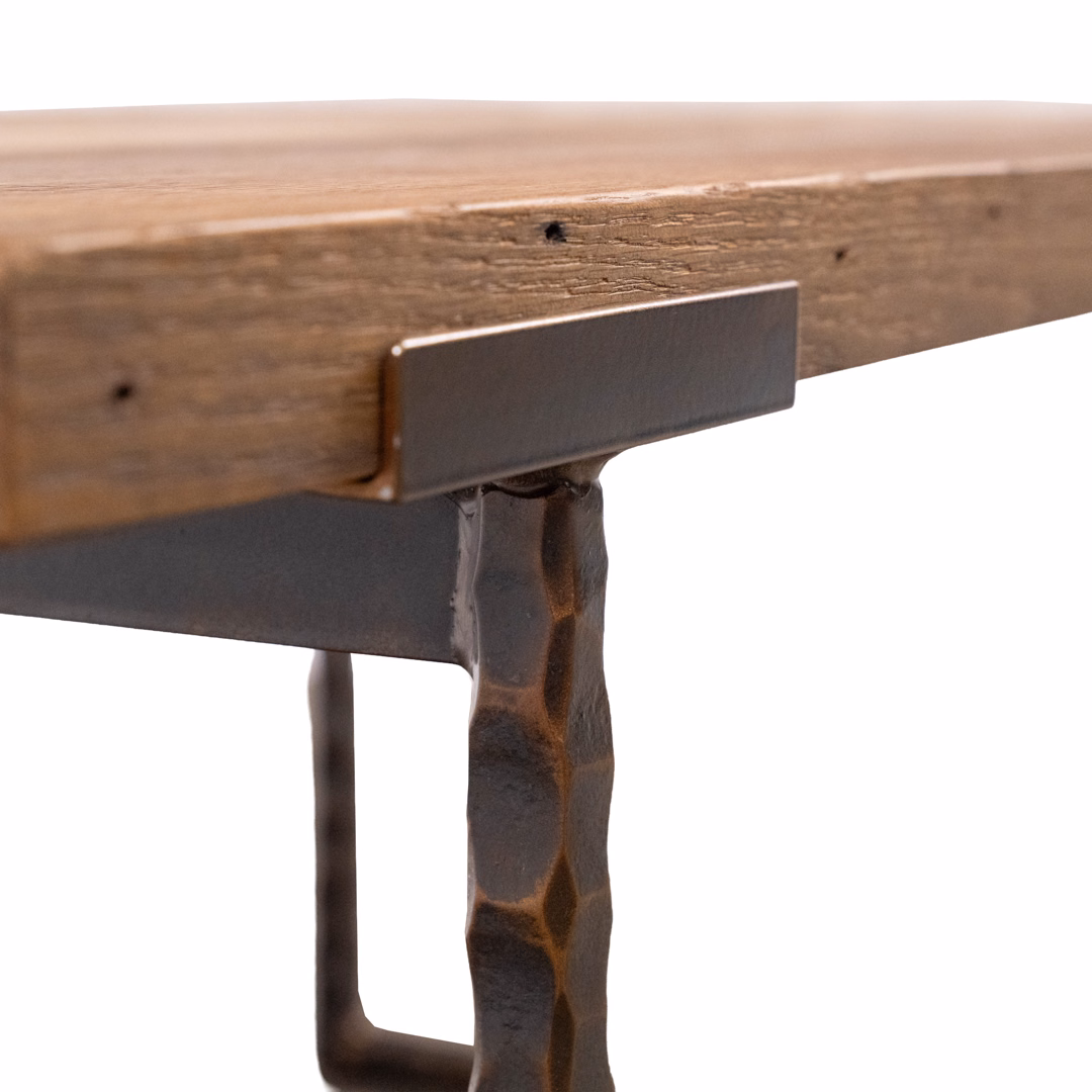 A close-up detail of a wooden tabletop connected to a textured dark metal leg with a metal support bracket.