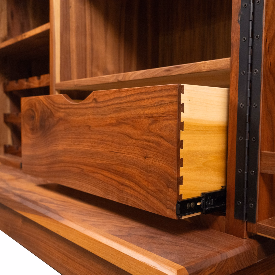 A close-up shot of a partially open wooden drawer with box joints and a black metal slide, integrated into a larger wooden cabinet.