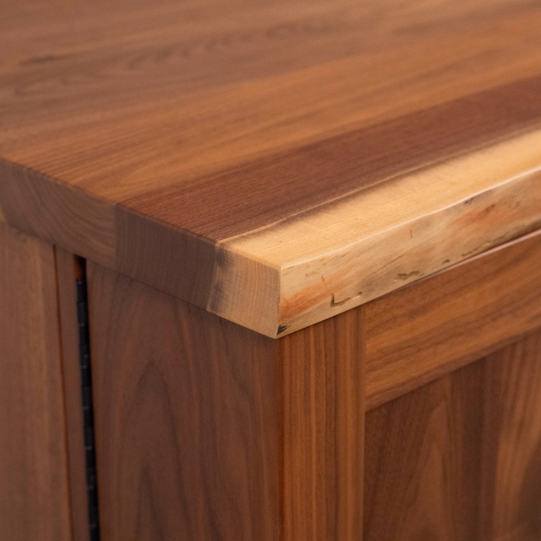Close-up of a light-brown wooden tabletop corner with a smooth finish and visible wood grain.