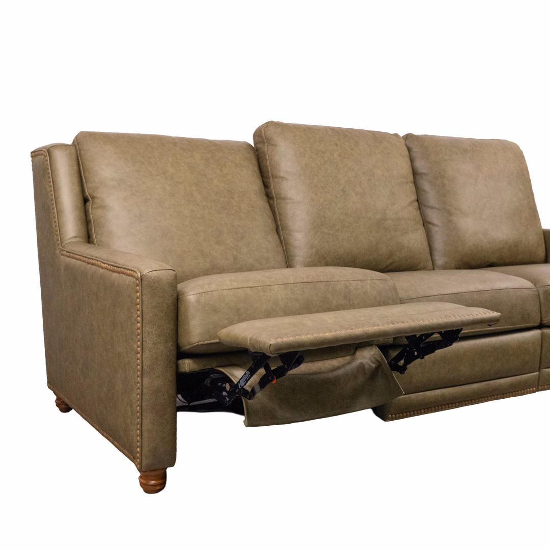 A beige leather-like reclining sofa with one footrest extended and decorative nailhead trim.